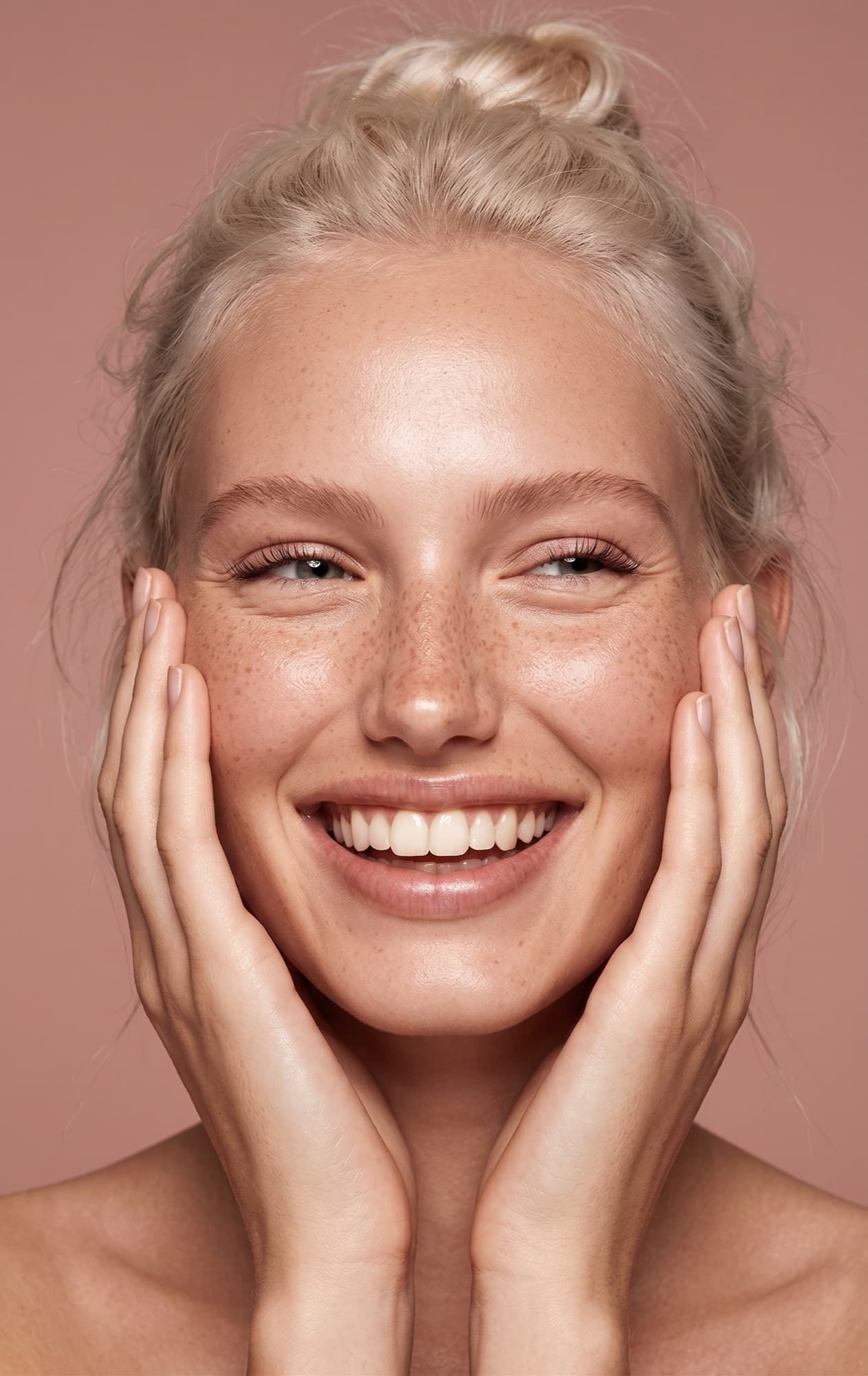 Laughing model framing her face with her hands on a dusty-pink backdrop
