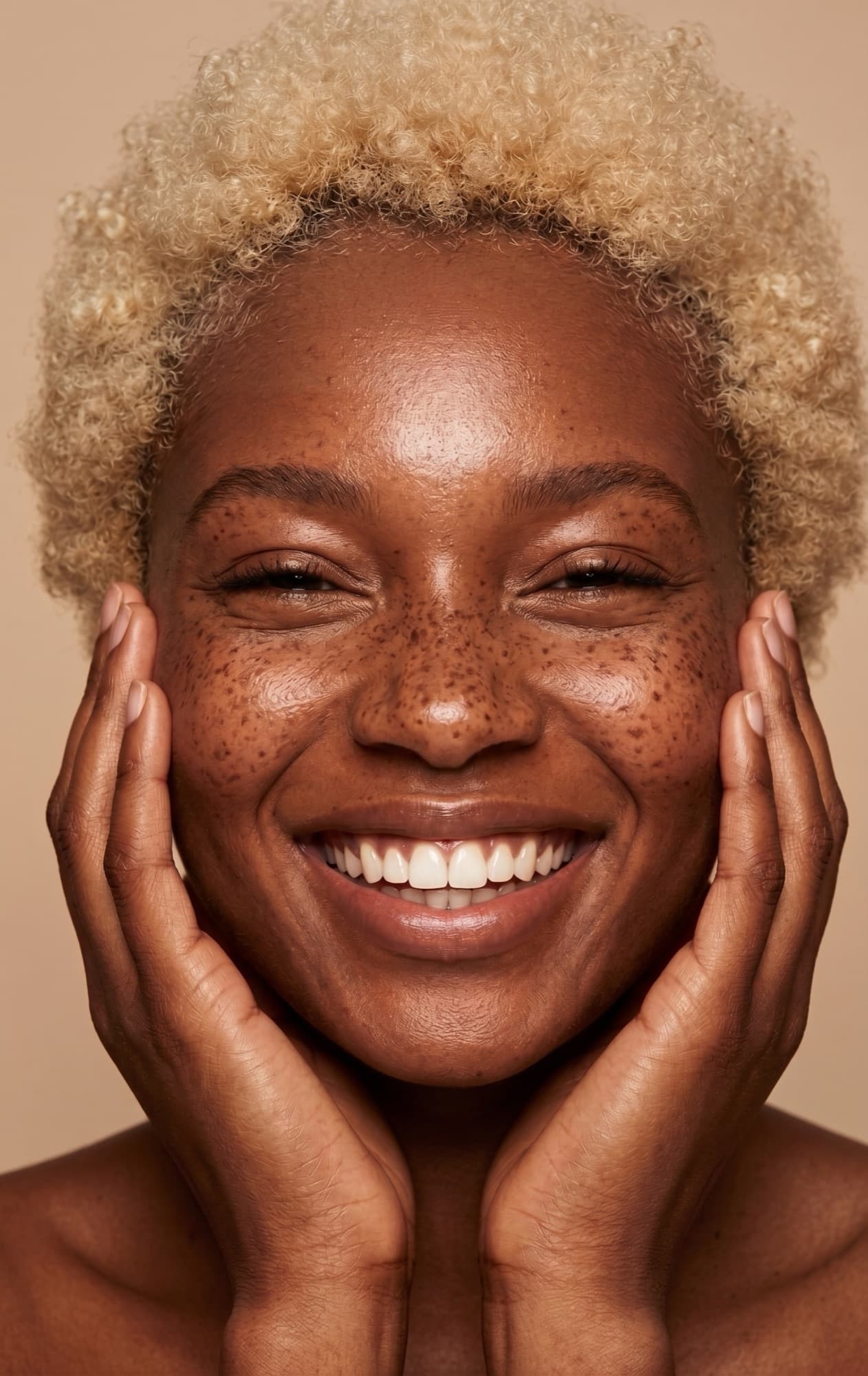 Smiling model framing her face with her hands on a warm beige backdrop